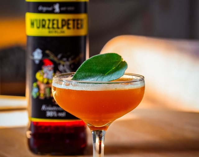 Ein elegantes Cocktailglas mit einem leuchtend orangefarbenen Getränk, garniert mit einem frischen Blatt.