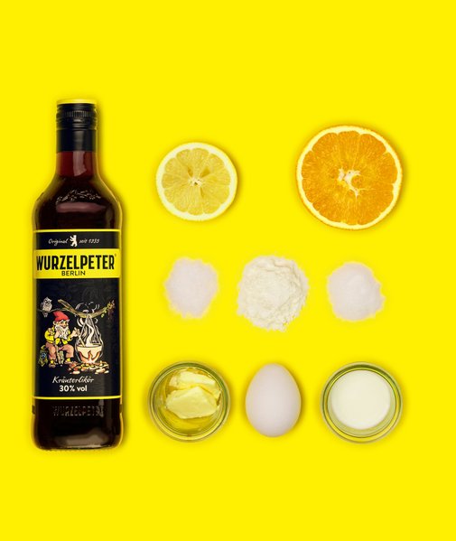 Eine Flasche Wurzelpeter steht auf einem leuchtend gelben Hintergrund, umgeben von frischen Zitronen- und Orangenscheiben.