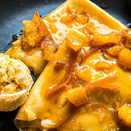 Leckere Pfannkuchen auf einem schwarzen Teller, überzogen mit einer süßen Sauce und frischen Früchten, begleitet von einem Likörglas.