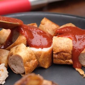 Auf einem schwarzen Teller liegen saftige Wurststücke, die mit rotem Ketchup garniert sind, bereit zum Genießen.